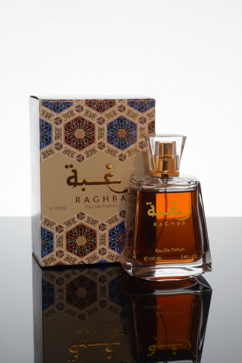 A bottle of Raghba Eau De Parfum with a faceted clear cap and amber-toned liquid, placed in front of its ornate patterned box. The packaging features Arabic calligraphy and a multicolor geometric tile design.