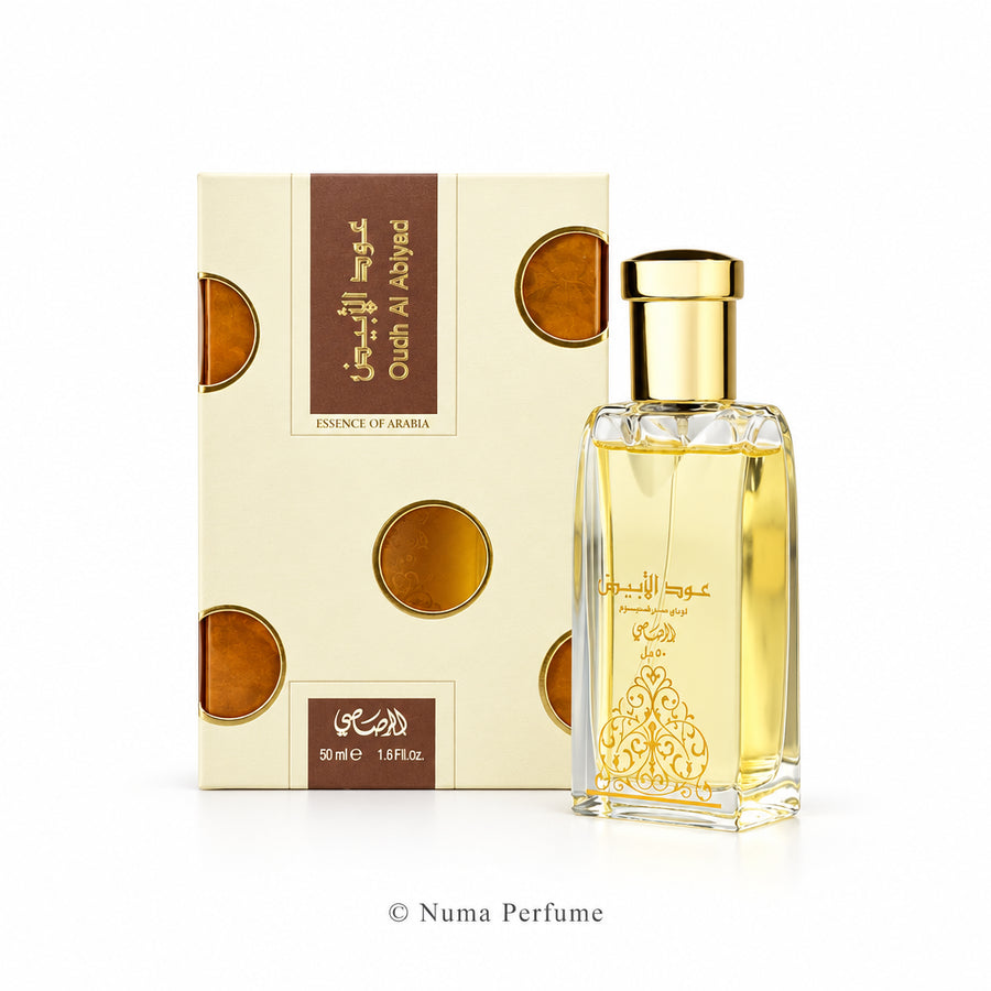 A bottle of Oud Al Abyad perfume with a gold cap next to its cream-colored packaging box with gold and brown accents, set against a plain white background.