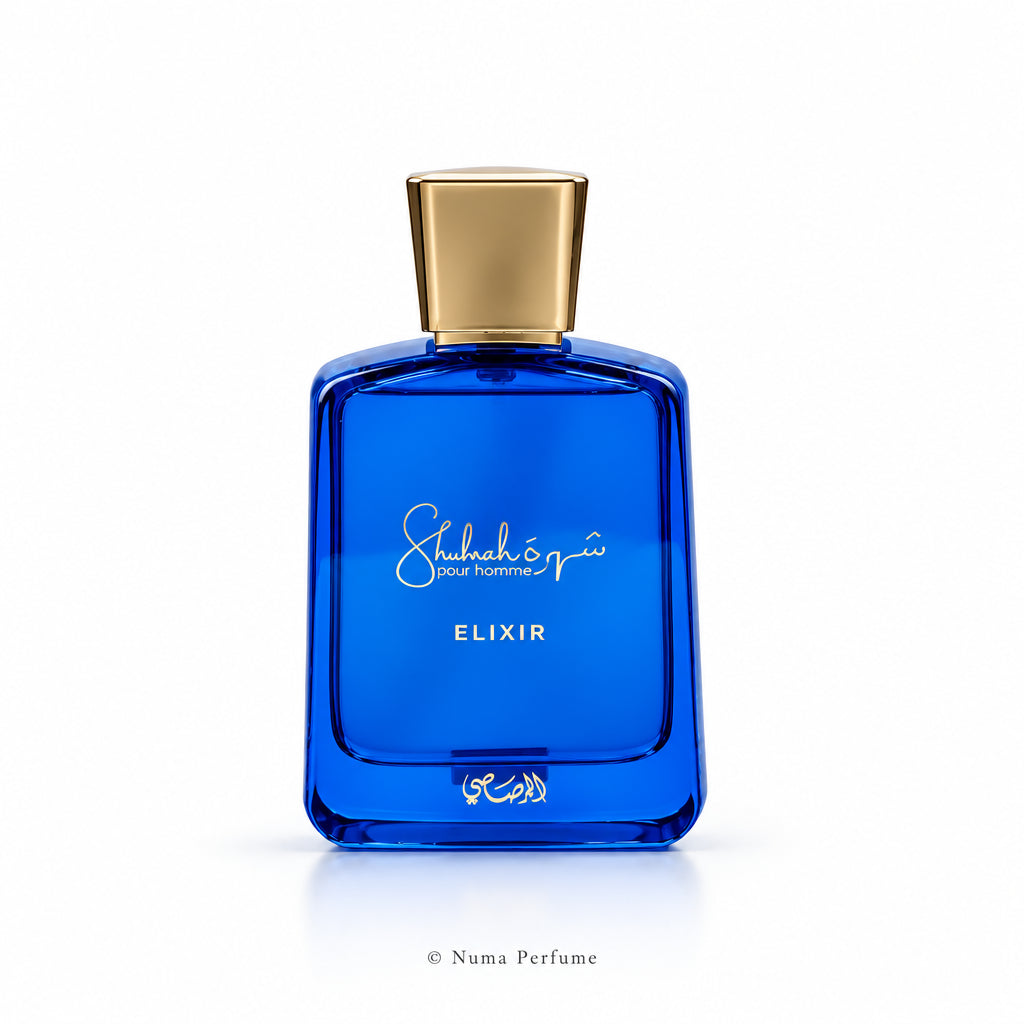 A blue glass perfume bottle with a metallic gold cap, featuring the brand name 'Shubhairi' and the product name 'ELIXIR' printed on the front, set against a plain white background.