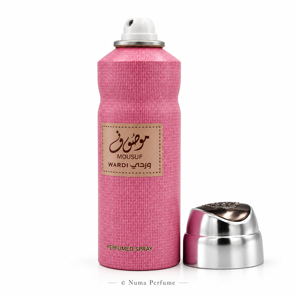 Pink perfume spray bottle with a white nozzle cap and a separate silver cap placed beside it on a white background. The bottle has a textured pink finish, a beige label with Arabic and English text reading MOUSUF and WARDI, and 'PERFUMED SPRAY' printed near the bottom.