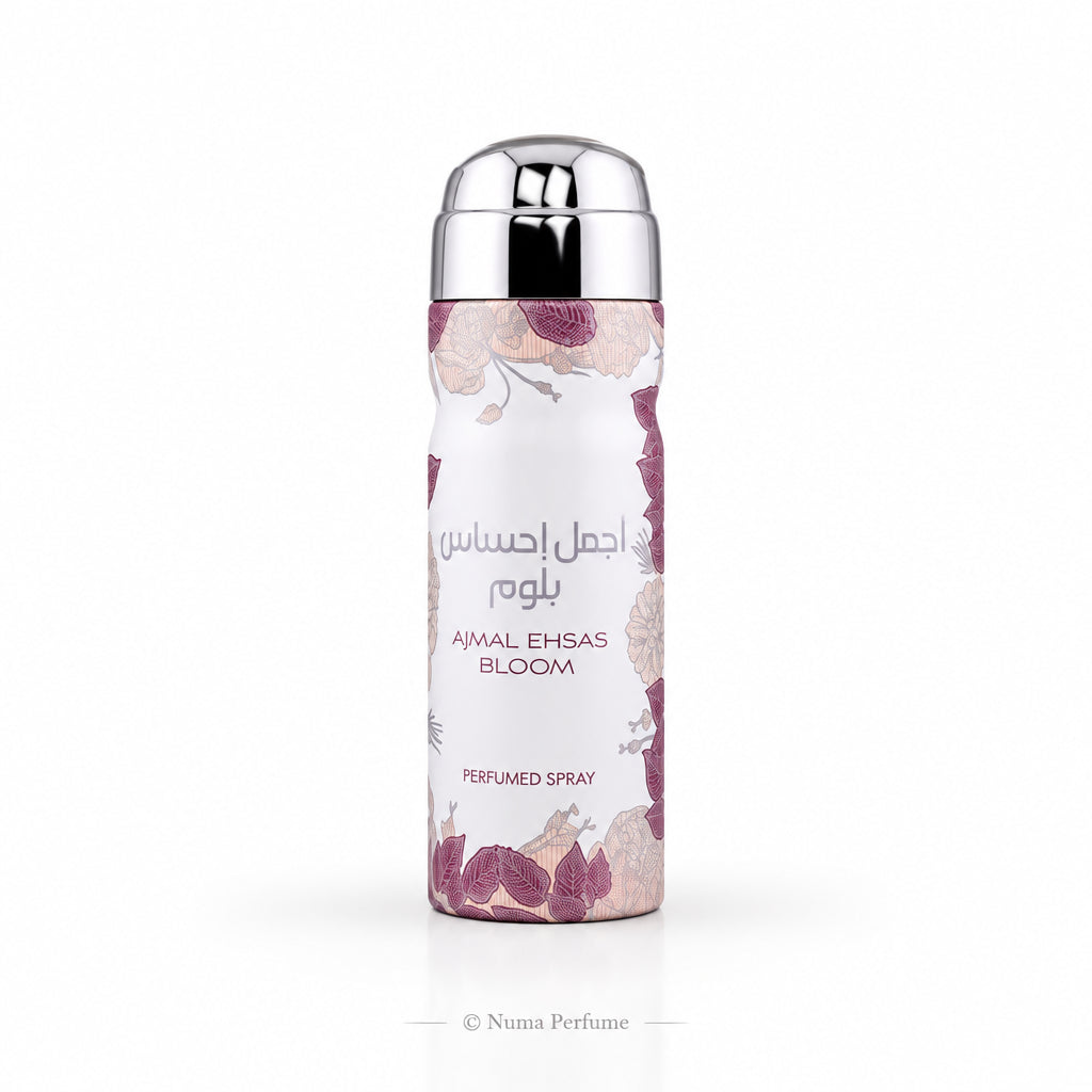 A cylindrical perfume spray bottle with a metallic silver cap and a white body decorated with pink and purple floral patterns. The Arabic text reads 'أجمل احسان' and 'AMAL EHSAS BLOOM' is printed below, with 'PERFUMED SPRAY' at the bottom.